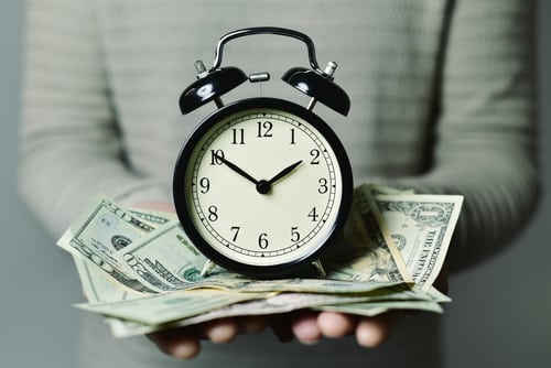 closeup of a young caucasian man with an alarm clock and many US dollar banknotes in his hands
