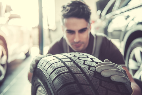 handsome young auto mechanic in uniform is examining a tire while working in auto service-img-blog